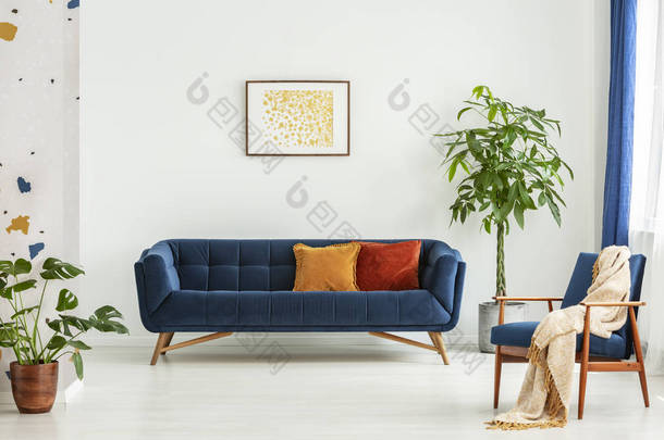中世纪现代椅子与毯子和<strong>一个</strong>大沙发与五颜六色的垫子在<strong>一个</strong>宽敞的客厅内部与绿色植物和白色墙壁。真实照片.