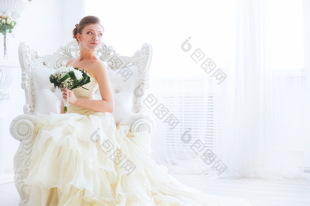 年轻的新娘坐在扶手椅上用鲜花.