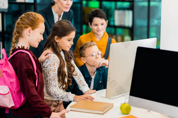 可爱的小学生和图书馆员一起使用计算机在图书馆 