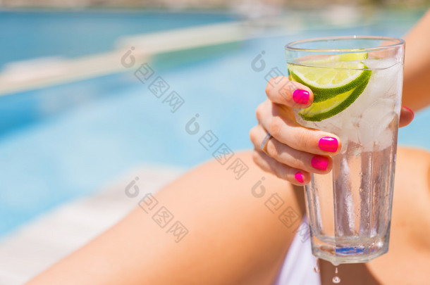 女人抱着在游泳池边晒日光浴时刷新冷饮料