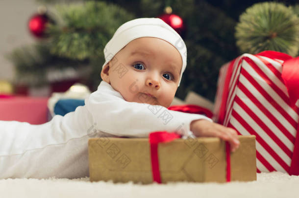 特写肖像可爱的小婴儿躺在地板上的圣诞礼物, 看着相机