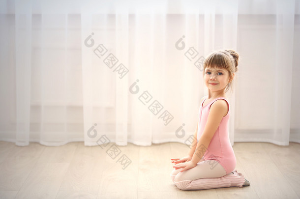 可爱的小女孩在粉红色紧身连衣裤，坐在地板上舞蹈工作室
