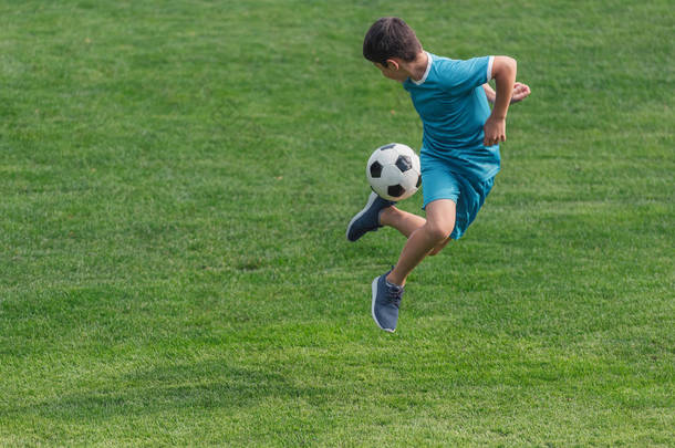 穿着运动服的孩子在绿草地上跳足球 
