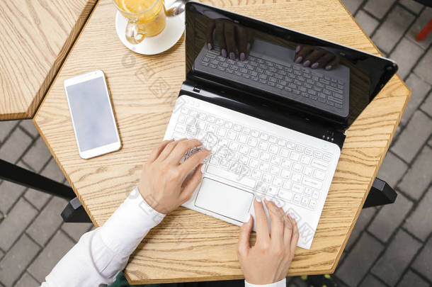 在夏季露台上的咖啡馆里做自由职业者的褐发女郎女商人。她喝茶, 并使用小工具作为笔记本电脑, 平板电脑和手机为她的工作。文本的空间。从上面看顶视图.
