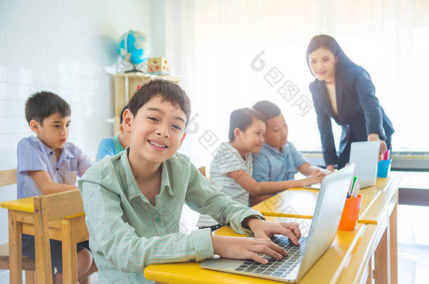 年轻的亚洲男孩使用膝上型电脑和微笑在教室里