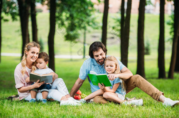 美丽的年轻家庭坐在草地上的公园和阅读书籍