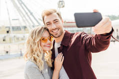 微笑的情侣在秋季服装采取自拍智能手机在城市