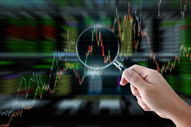 Hand holding magnifying glass with stock market graph background