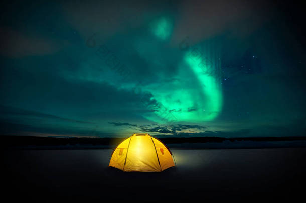 在荒野中, 诺什的灯光 (极光) 在瑞典的夜空中翩翩起舞, 上面是露营帐篷里发光的灯光。照片合成.