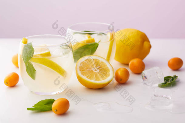 两杯柠檬水与薄荷叶, 冰块和<strong>柠檬片</strong>包围的金橘和柠檬在紫色的背景下 