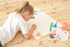 女孩躺在地板上绘画用品和绘画在白纸上