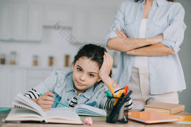 部分视图的妇女站在交叉的手臂背后无聊的女儿做家庭作业
