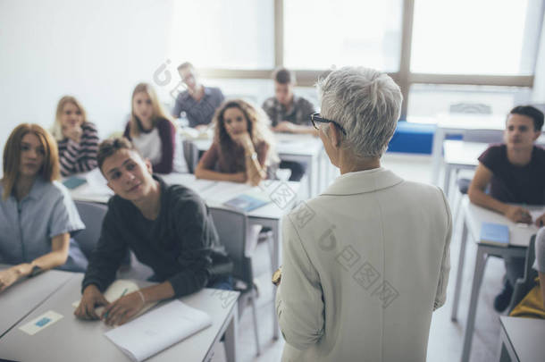 灰色头发女<strong>教师</strong> stading 在课堂上的背观与高中生的谈话.