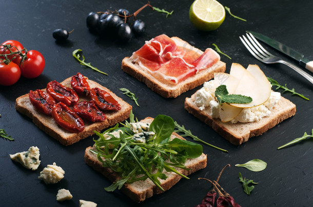 Sandwiches with a variety of toppings on a dark surface. Sandwiches with arugula, leaf mash, blue ch