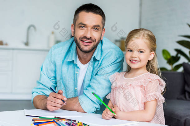 愉快的父亲和女儿<strong>画</strong>与彩色铅笔和微笑在照相机