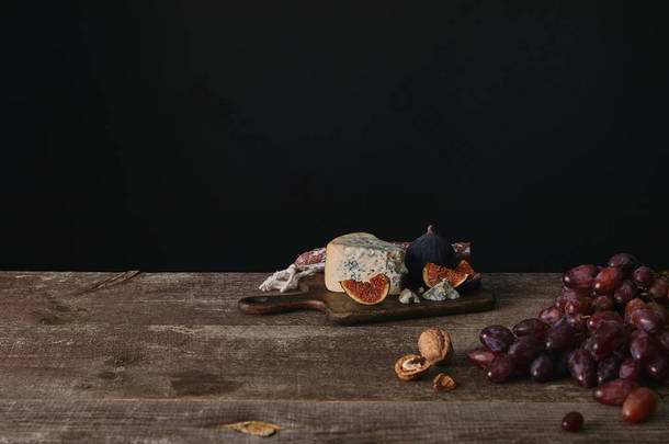 新鲜成熟的葡萄, 坚果和美味的奶酪在木桌上的黑色