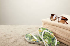 在灰色背景下, 对沙滩上的毛巾、太阳镜和夏季翻转的拖鞋进行特写查看