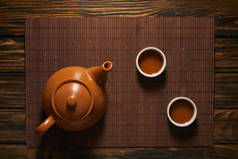 在竹垫上可以看到棕色陶瓷茶壶和茶杯的顶视图