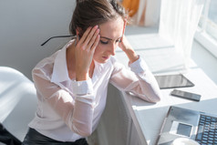 累了的年轻商界女强人患头痛在前面笔记本电脑在办公桌的肖像