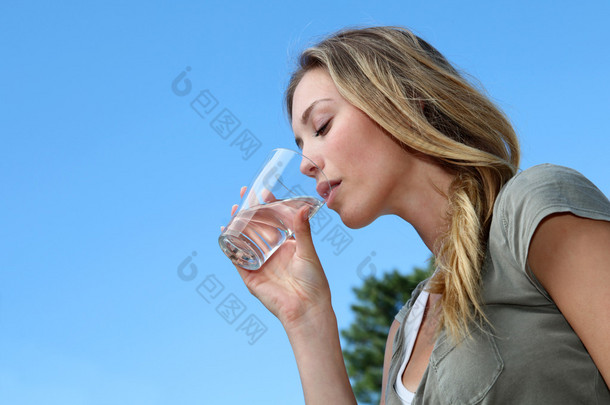 玻璃的金发碧眼女人饮用水的特写