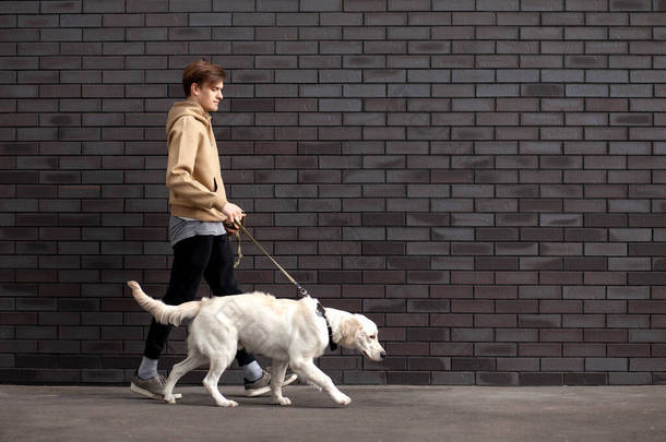 一个年轻的小伙子，带着一只狗在街上靠着墙走