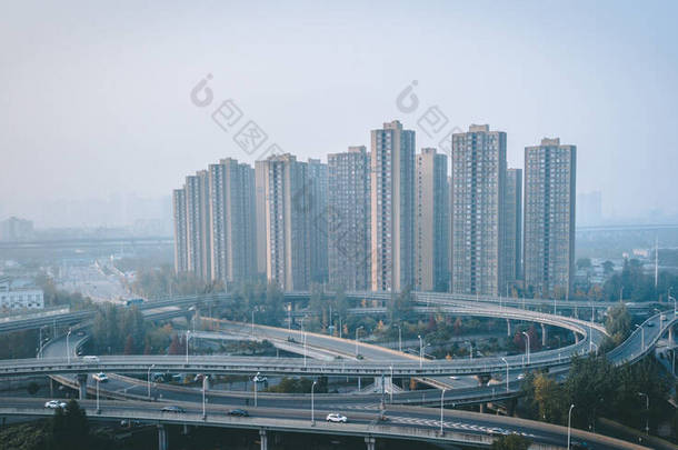 巨大的建筑物将高耸的公路交通交汇处夷为平地，旁边耸立着几层高的摩天大楼。成都东部，成化地区。严重的空气污染、不健康的空气污染.