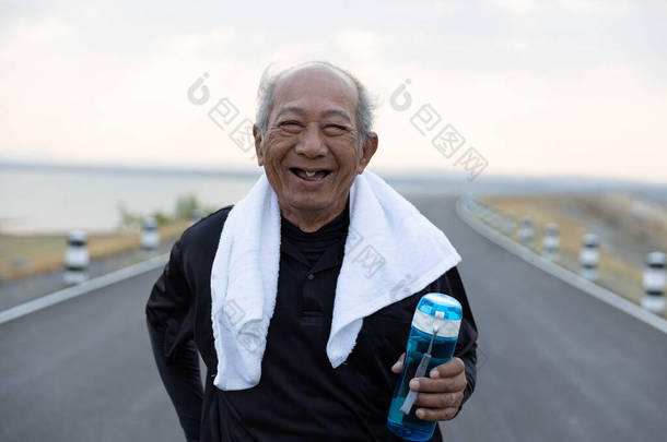 前瞻亚洲老年人运动快乐的微笑,积极向上的情感.在早晨的阳光下,把老人抱在路上的<strong>水瓶</strong>关上.健康生活方式和运动概念.