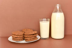牛奶装在玻璃瓶中，透明玻璃和饼干装在白色盘子上