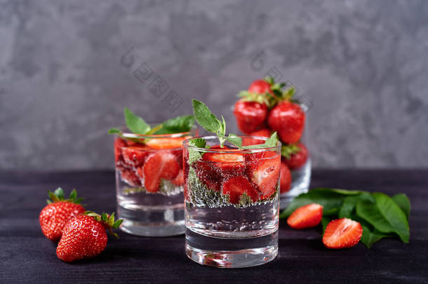 将草莓和薄荷糖倒入水中，用闪闪发光的玻璃杯在木黑色桌子的背景上，复制空间。寒冷的夏季饮料。<strong>矿泉水</strong>