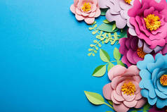 彩色剪纸花与绿叶在蓝色背景与复制空间的顶视图