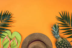 菠萝，热带叶子，绿色拖鞋和棕色草帽在橙色背景与复制空间的顶视图