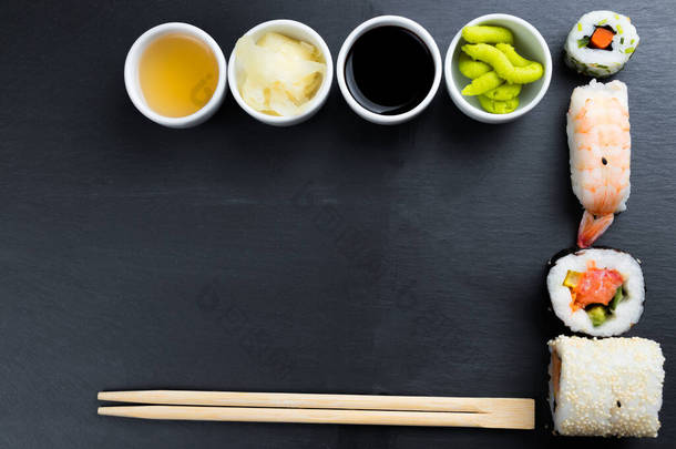 典型的亚洲菜设置在黑色厨房板上.<strong>生姜</strong>、日本辣椒酱、芥末、酱油和鱼露在小白碗里.筷子。Sushi - futomaki和nigiri 。帧中的复制空间.