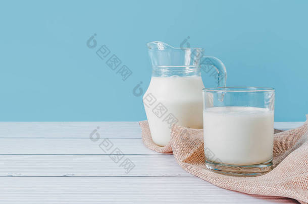 天然<strong>鲜牛奶</strong>在玻璃杯和水壶里，放在餐巾上，放在蓝色背景的木制桌子上。饮食促进健康