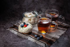 茶在透明的杯子里，有亮点，蒸汽，糖碗里有块糖，蛋糕上有草莓和蓝莓，背景是灰色的