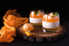 奶油智慧, 橙色果冻在美丽的眼镜, 新鲜成熟的普通话在黑色背景的木制部分。美味的意大利甜点。现代黑暗情调风格.