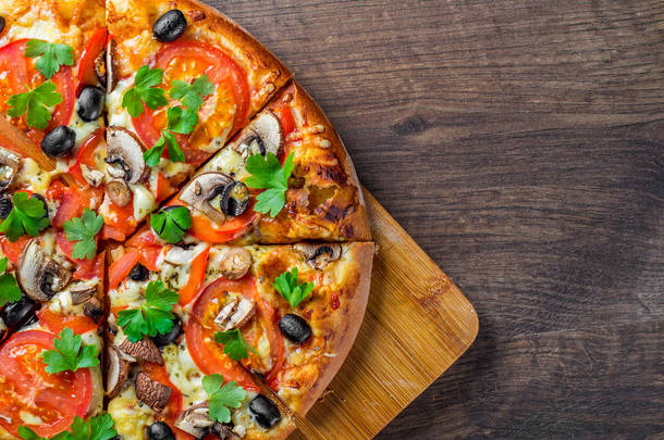 切片披萨与莫扎雷拉奶酪，番茄，胡椒，橄榄，蘑菇，香料和新鲜叶。木制餐桌上的意大利披萨