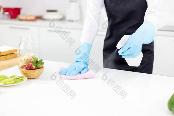 漂亮的美女或家庭主妇在厨房的餐桌上擦拭、清洁、喷涂防腐剂或消毒剂。清洗能杀灭病菌、细菌。迷人的美丽的女孩戴手套, 围裙.