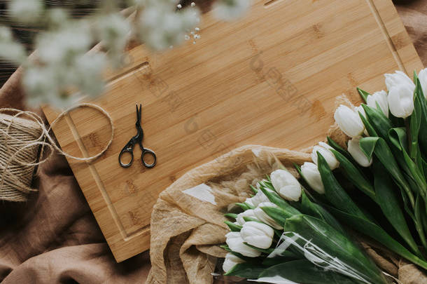 3月8<strong>日</strong>木制木板上的白色郁金香、剪刀和麻线的顶部视图