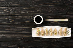筷子附近盘子里美味的中国水饺和黑树林里的酱油俯视图