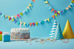 美味的生日蛋糕, 礼物, 派对帽和五彩纸屑蓝色背景与彩带
