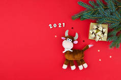 公牛是2021年新年的象征。红色节日背景上的毛绒玩具，有冷杉枝条和礼物。中国农历2021年牛年.