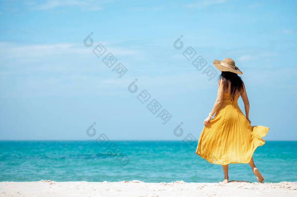 暑假。生活风格的女人在海滩背景上放松和冷静.亚洲快乐的年轻人穿着黄色衣服参加夏天的时尚旅行,漫步在热带海滩上.生活方式和旅行概念.  