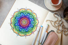 彩色曼陀罗艺术书籍的顶部视图，带有彩色标识、钢笔、粉色笔盒和念珠。将曼德勒涂色作为冥想技巧的概念.