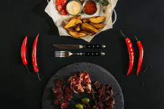 烤土豆酱, 辣椒, 叉子, 刀和美食的顶级视图黑色石板板上的各种肉