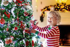 孩子们在家里装饰圣诞树。穿着睡衣、戴着圣诞装饰品的小男孩。有孩子的家庭庆祝寒假。孩子们在圣诞节装饰客厅和壁炉.