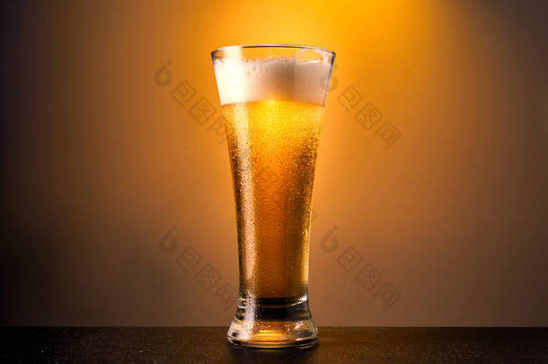 冷工艺的淡啤酒在玻璃杯中,滴滴在黑暗的桌子上.一品脱啤酒加黄色底色.靠近点.
