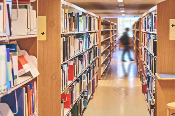 学生在图书馆书架之间通过一个通道走