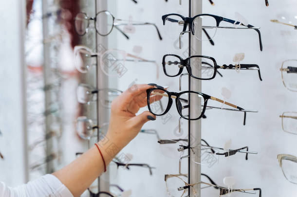 选择的眼镜。光学的客户。有选择地集中在手上。女人拿着眼镜站着摸矫正眼镜.商店里各种各样的商品.