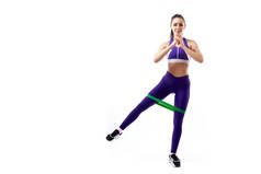 一个在运动紫色短上衣和健身房紧身裤的伊蓬女子教练在脚前冲刺与运动健身橡皮筋, 舒展腿在白色隔离的背景在演播室 