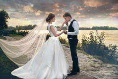 新娘和新郎在婚礼礼服上的自然背景。新婚夫妇在日落时分沿着河岸散步。.